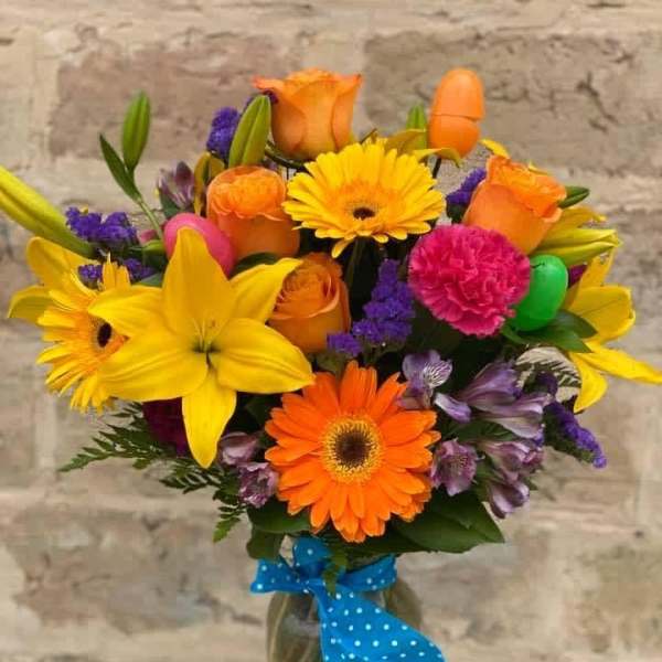 Bright mixed bouquet in a glass vase with a blue polka-dot ribbon