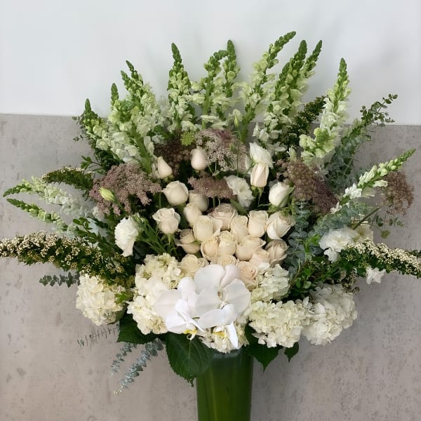 Tall white floral arrangement in a green glass vase