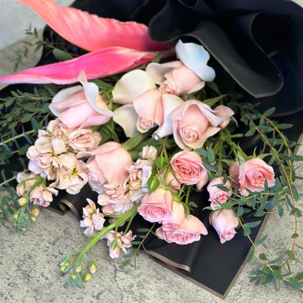 Bouquet of pale pink roses and pink calla lilies wrapped in black paper