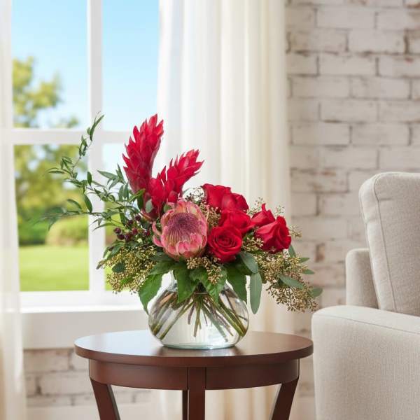 Red floral arrangement in a clear glass vase on a side table