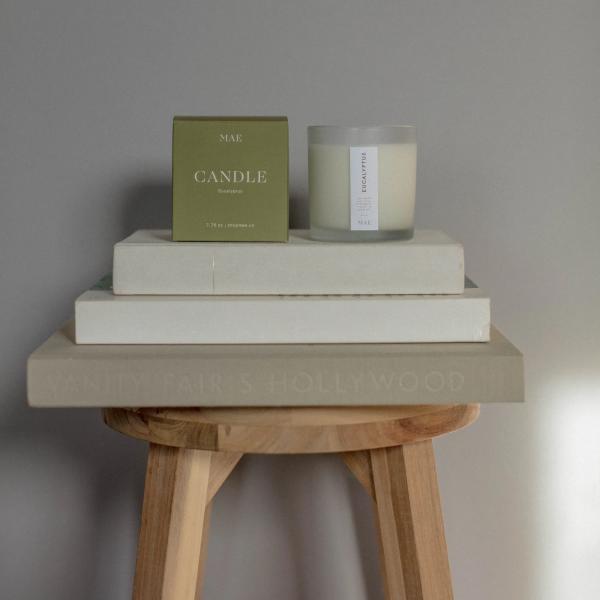 Eucalyptus candle in a glass jar beside its box on stacked books