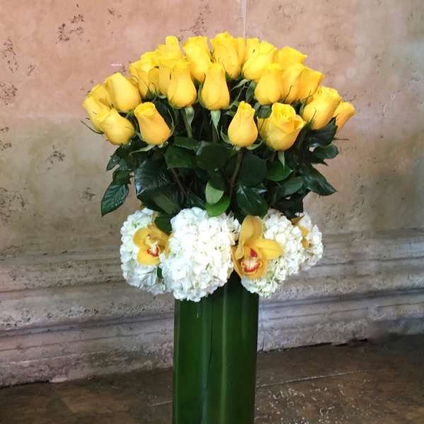 Yellow roses and white orchids arranged in a tall green vase