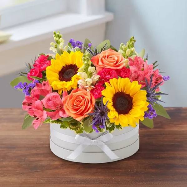 Bright mixed flower arrangement in a white round box with ribbon