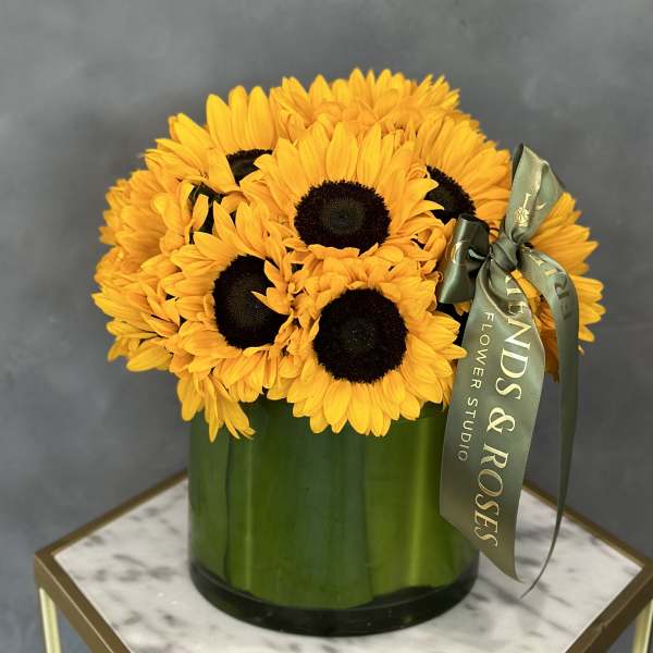 Bouquet of yellow sunflowers in a green glass vase with a ribbon