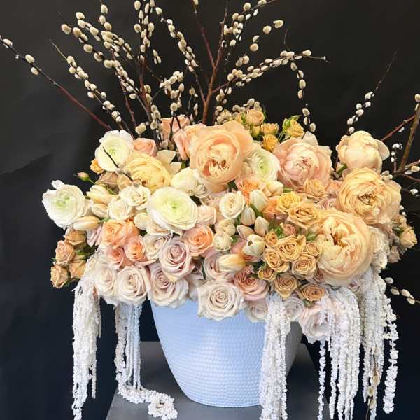 Large peach and cream floral arrangement in a white vase with tall branches