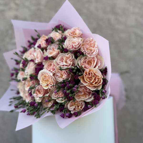 Bouquet of pale pink roses with purple filler flowers in pink wrapping