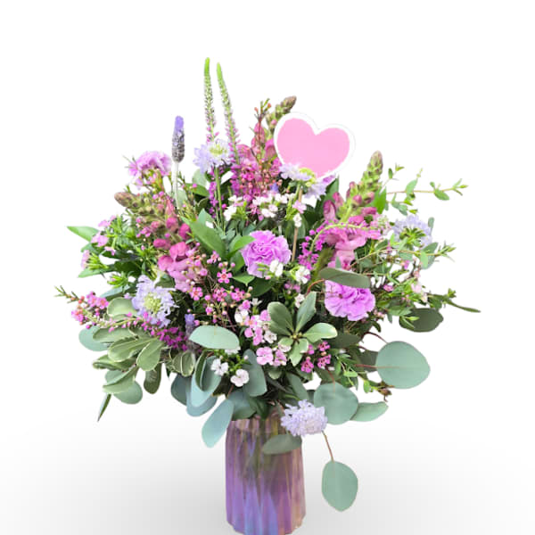 Pink and lavender mixed bouquet in a purple glass vase with a heart pick