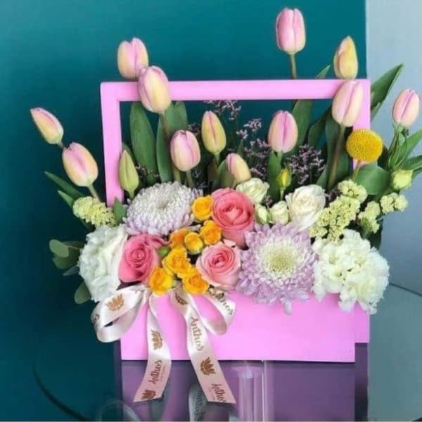 Pink tulips and mixed flowers arranged in a pink box with a ribbon