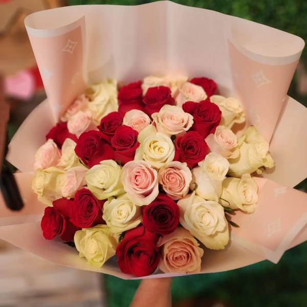 Bouquet of red, white, and blush roses wrapped in pale pink paper