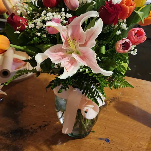Bouquet of lilies, roses, and tulips in a glass vase with a ribbon