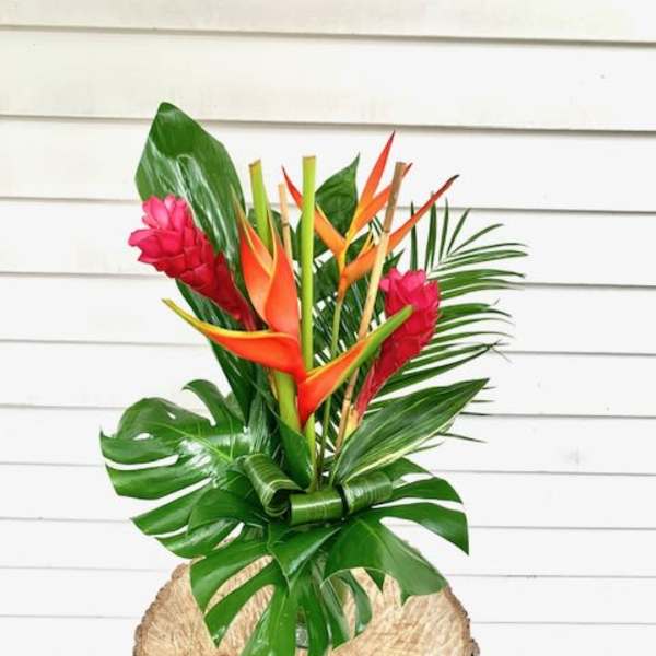 Tropical arrangement with orange heliconia and pink ginger in a rustic wood container