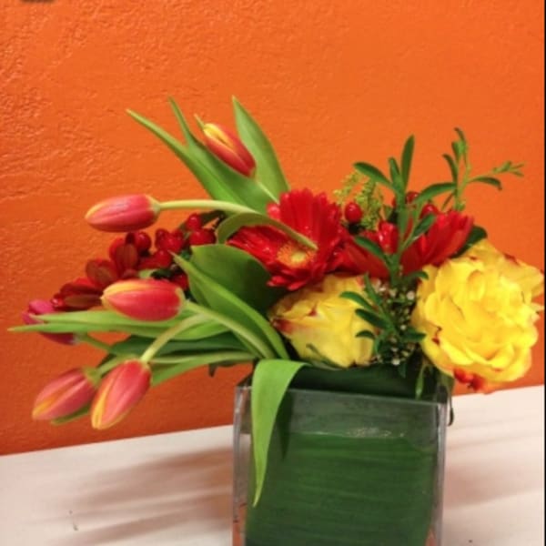 Colorful bouquet of tulips, roses, and gerbera daisies in a square glass vase