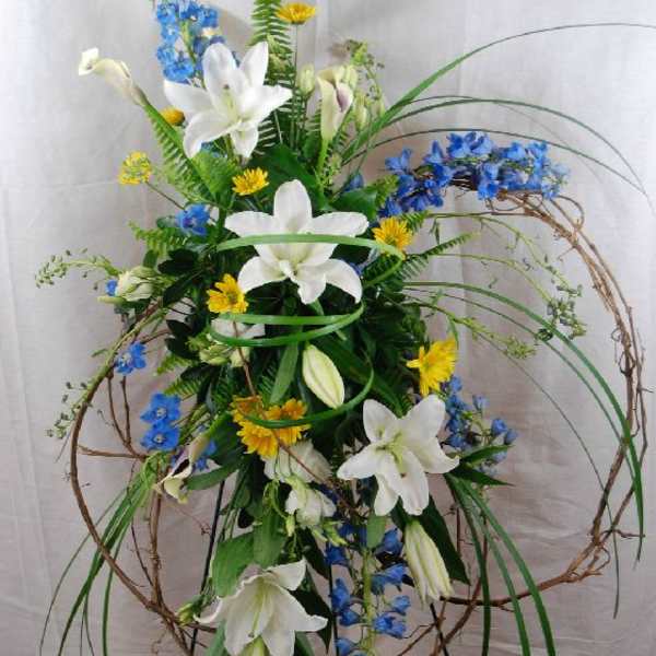 Tall floral arrangement with white lilies, blue flowers, and yellow accents on a stand