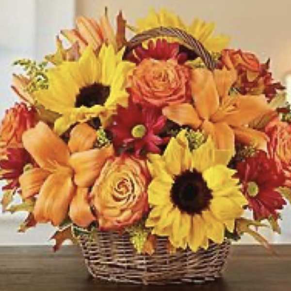 Basket arrangement of sunflowers, lilies, and roses in orange and yellow tones