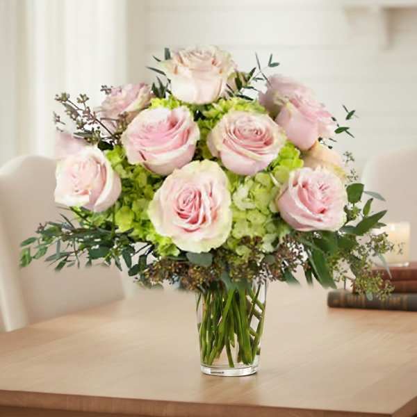 Arrangement of pale pink roses and green hydrangeas in a clear glass vase on a table