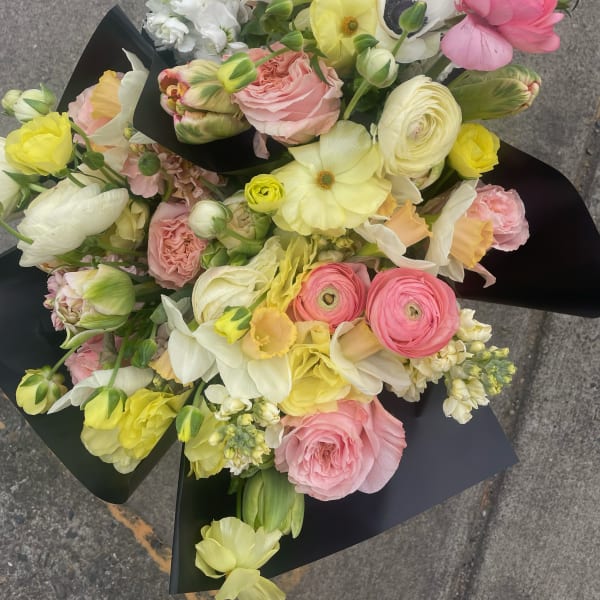 Mixed bouquet of pink, yellow, and white flowers wrapped in black paper