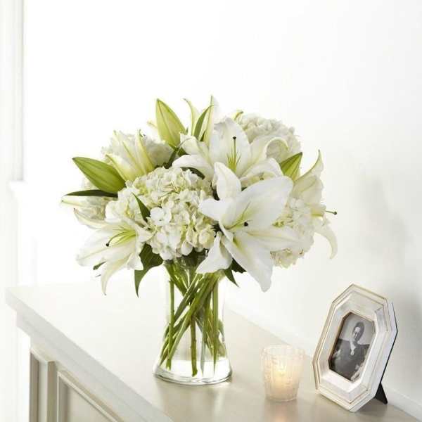 White lilies and hydrangeas in a clear glass vase on a table.