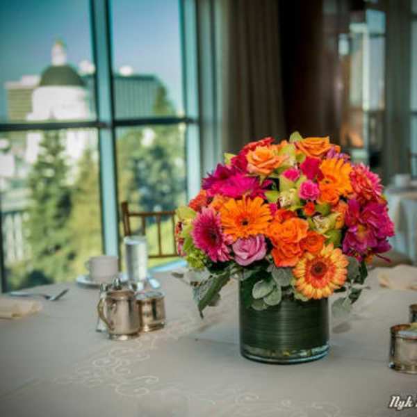 Round centerpiece of bright orange and pink flowers in a glass vase on a banquet table