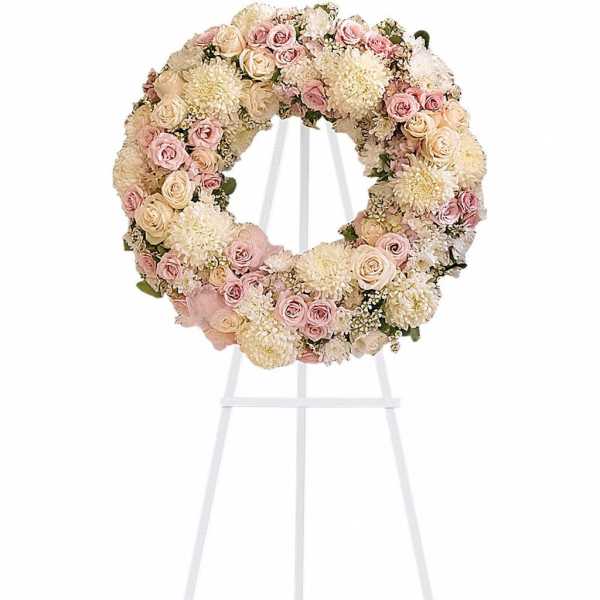 Pastel pink and cream floral wreath displayed on a white metal easel stand