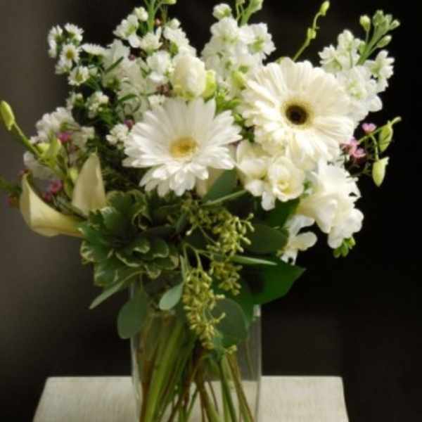White gerbera daisies and mixed white flowers in a clear glass vase