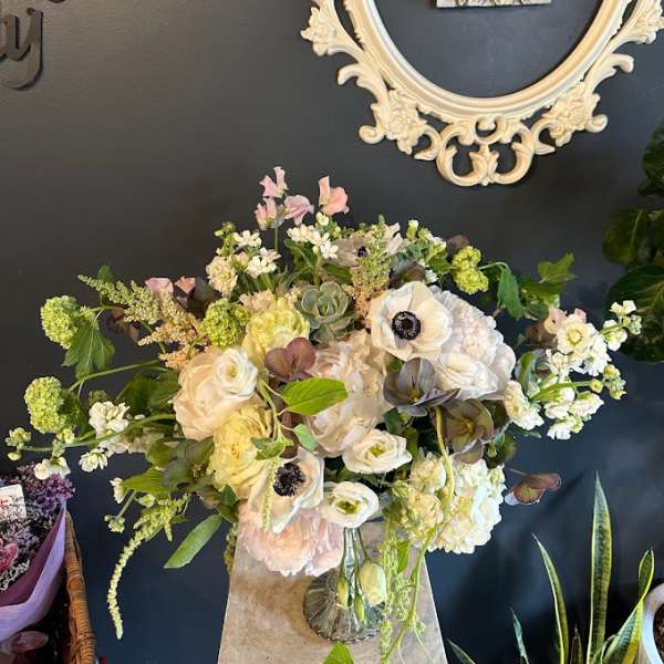Large mixed floral arrangement in a glass vase with cream and pale pink blooms
