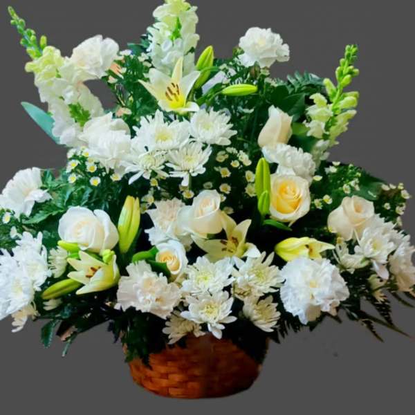 White floral arrangement in a woven basket with lilies and roses