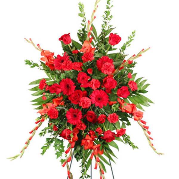Tall standing spray of red roses, gerbera daisies, carnations, and other red blooms on a metal easel