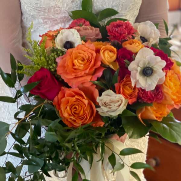 Bride holding a bouquet of orange, pink, and white flowers with trailing ribbon