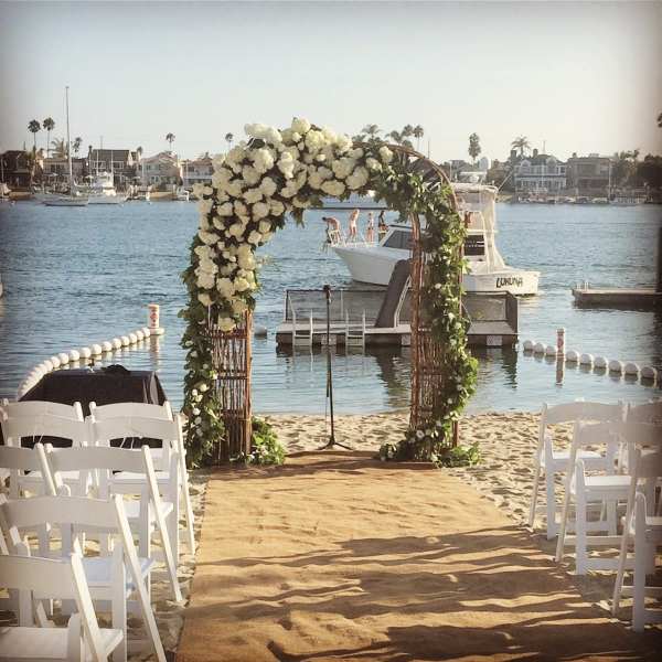 White floral arch on a beach aisle with chairs facing the water