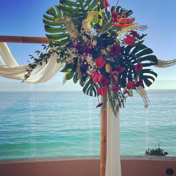 Tropical floral arch with red blooms and white draping by the ocean