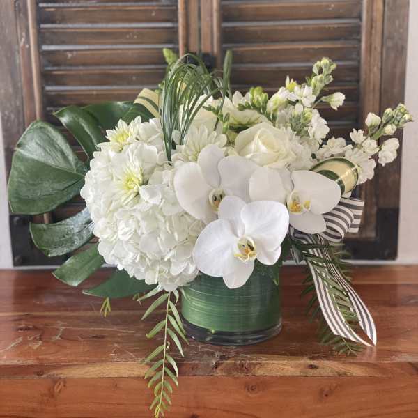 White floral arrangement with orchids, hydrangeas, and roses in a green vase