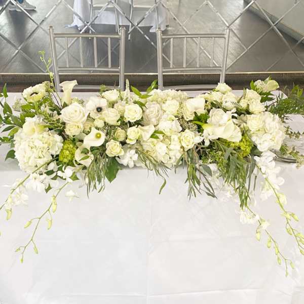 Long white floral table arrangement with roses and calla lilies