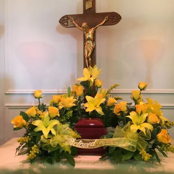 Yellow floral arrangement around a red urn beneath a crucifix