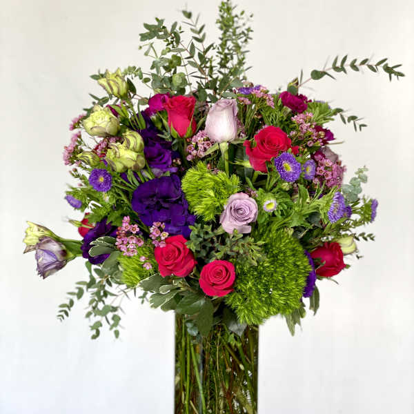 Tall bouquet of pink, purple, and green flowers in a gold vase