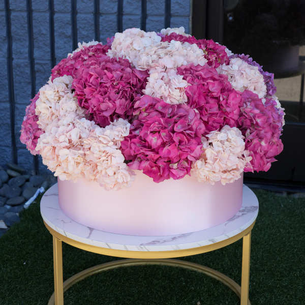 Large pink and white hydrangea arrangement in a round box on a gold table