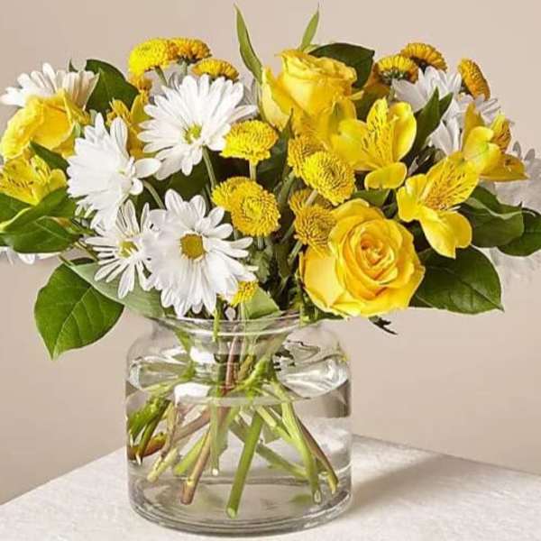 Yellow roses and white daisies in a clear glass vase