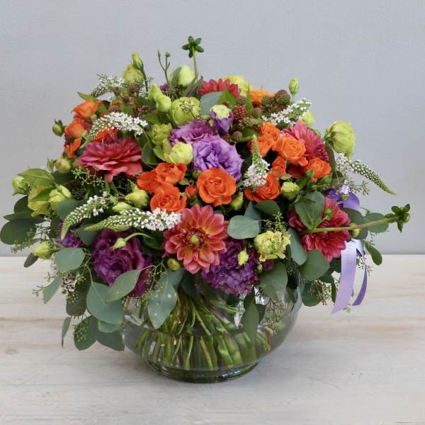 Low round arrangement of orange and purple flowers in a clear glass bowl vase