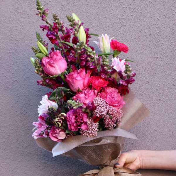 Hand-tied bouquet of pink and magenta flowers wrapped in brown paper