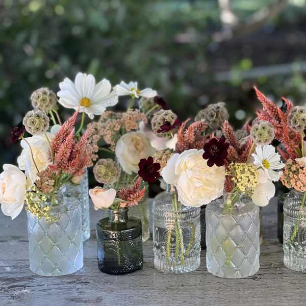 Small mixed flower arrangements in assorted glass bottles on a table