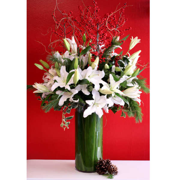 White lilies in a tall green vase with red berry branches