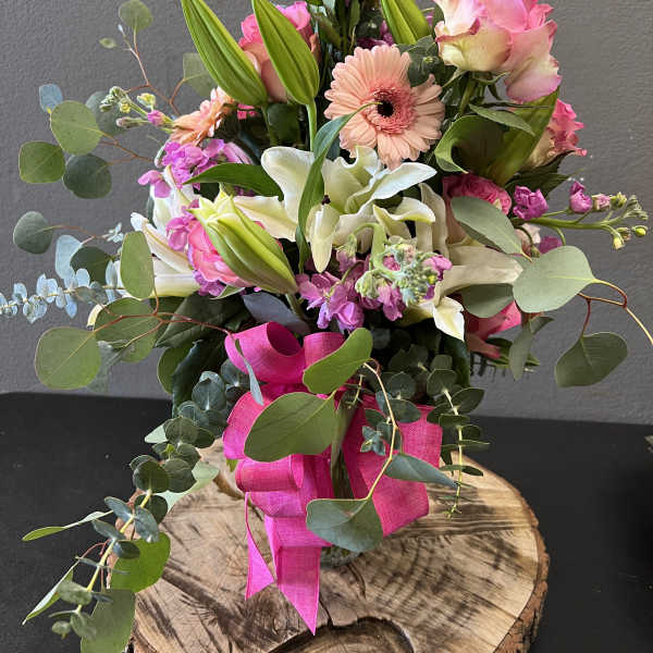 Pink roses, lilies, and a gerbera daisy in a glass vase with a pink ribbon