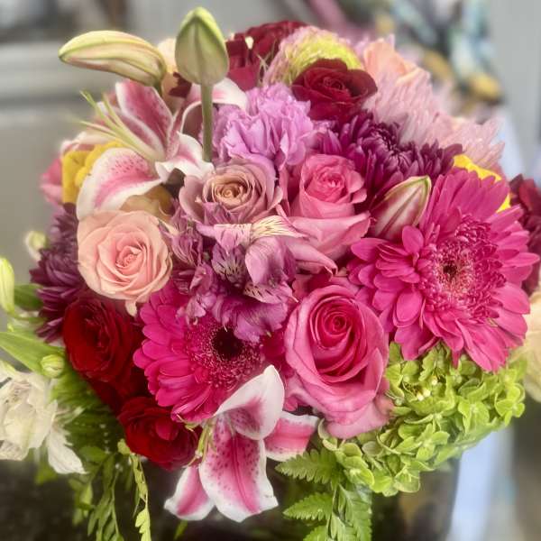 Round bouquet of pink lilies, roses, gerbera daisies, and green hydrangeas in rich pink and red tones