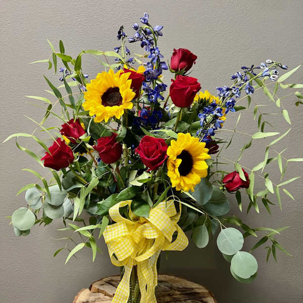 Bouquet of red roses and sunflowers in a glass vase with a yellow ribbon