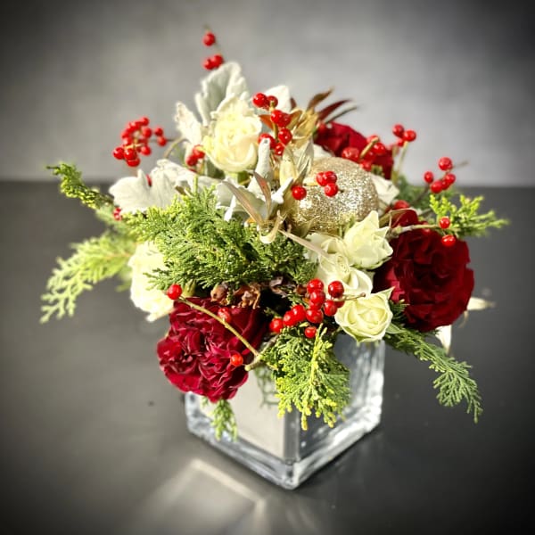 Red and white roses arranged in a clear square vase with berries
