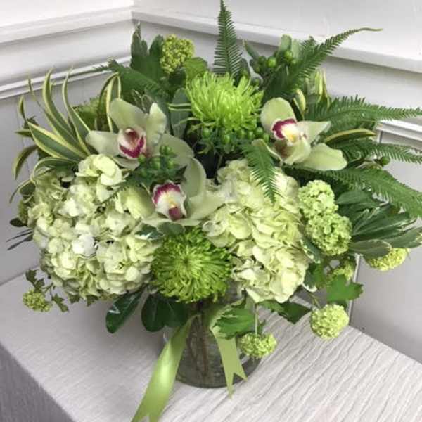 Green floral arrangement with orchids and hydrangeas in a glass vase