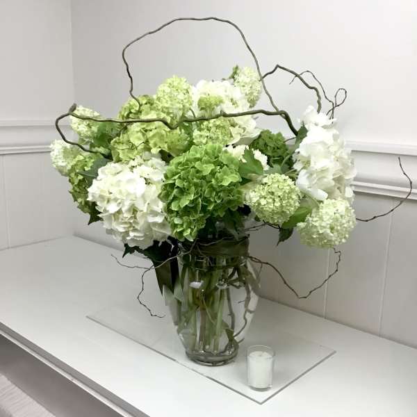 White and green hydrangea arrangement in a glass vase with curly branches