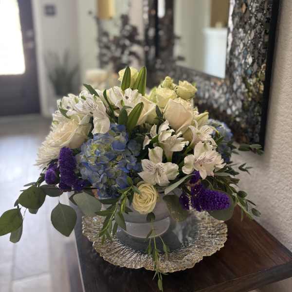 Mixed bouquet in a low silver bowl with cream, blue, and purple flowers