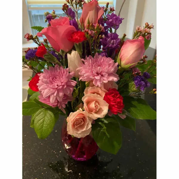 Mixed bouquet of pink roses, chrysanthemums, and purple flowers in a vase