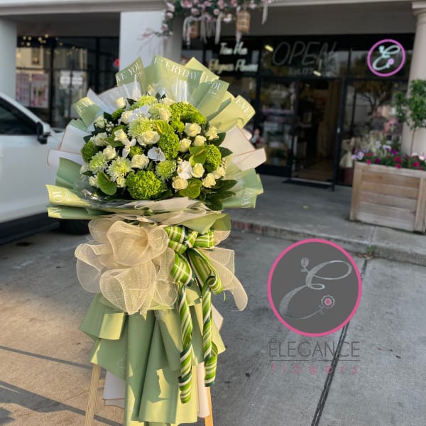 Large bouquet of white and green flowers wrapped in green paper with a bow