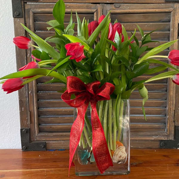Red tulips in a clear glass vase with a red ribbon